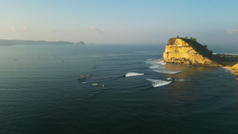 Vista-Aérea-Panorámica-Del-Lugar-De-Surf-De-Gerupuk-Con-Surfistas-Montando-La-Ola,-Acantilados-En-Medio-Del-Mar-De-Bali