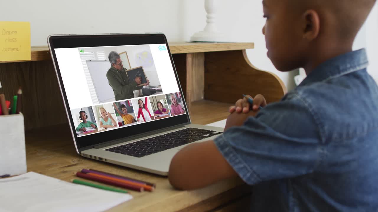 Schoolboy using laptop for online lesson at home, with diverse teacher and class on screen