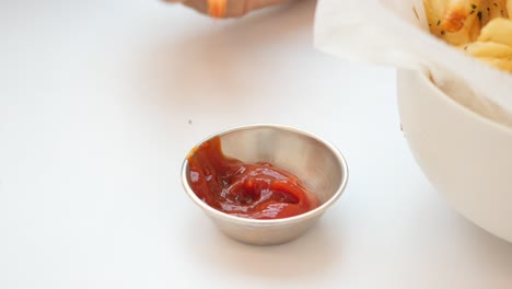 persona sumergiendo papas fritas en ketchup