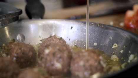 close up of pouring vegetable broth into pan of meatballs preparing ingredients to make vegan beyond meatballs with spaghetti and meat sauce