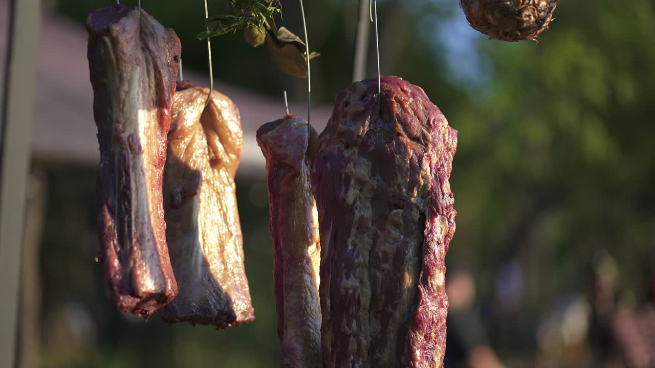 Raw ribs hanging and seasoned with salt and pepper, ready for the asado, a traditional barbecue from argentina, chile, paraguay, and uruguay, slow motion shot, oof background with bokeh effect