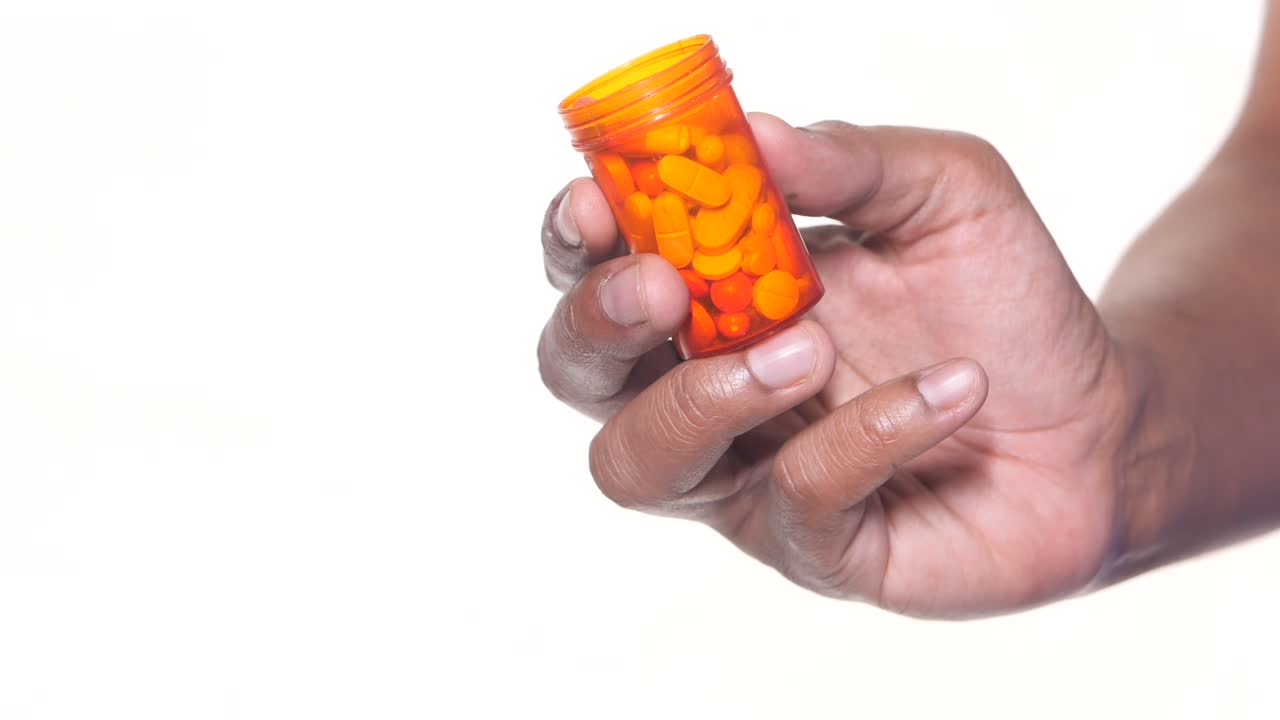 Hand holding an orange pill bottle with pills inside