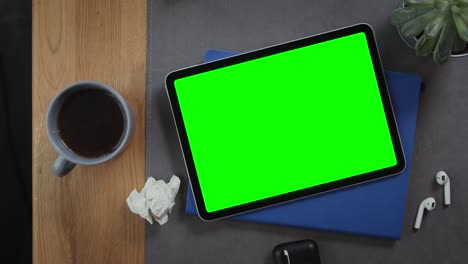 a tablet with a green screen lies on the desktop next to a cup of hot tea