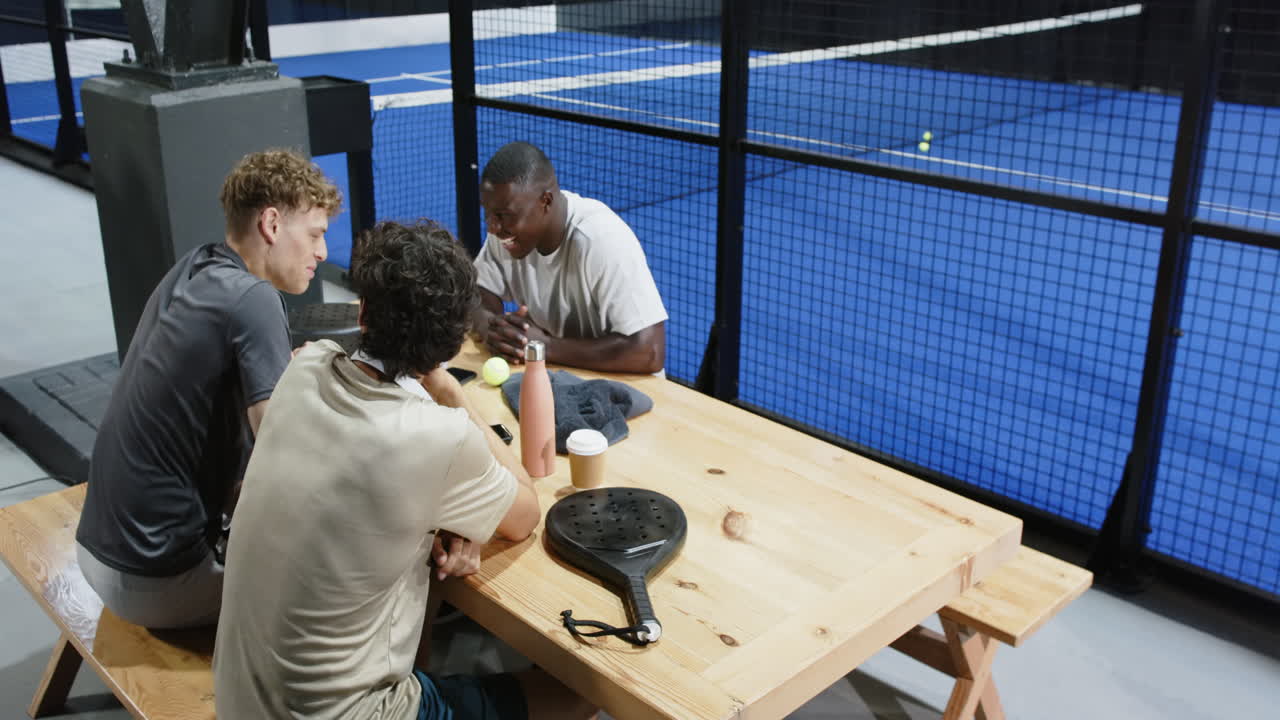 Diverse friends celebrating after padel tennis match, enjoying time together, on indoor court