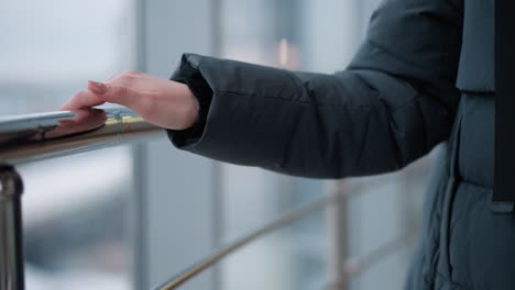 primer plano de la mano de la mujer con anillo deslizándose en el carril brillante mientras camina a través de un edificio moderno con reflejos de vidrio y luces parpadeantes en el fondo