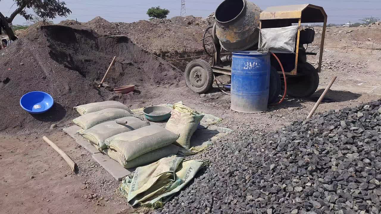 Footage of concrete mixer machine, sand, cement bags, and crusher stone kept at the construction site for new building construction - Construction materials