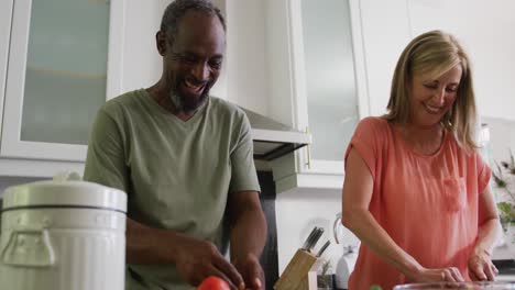 Happy-diverse-senior-couple-preparing-food-in-kitchen-and-talking
