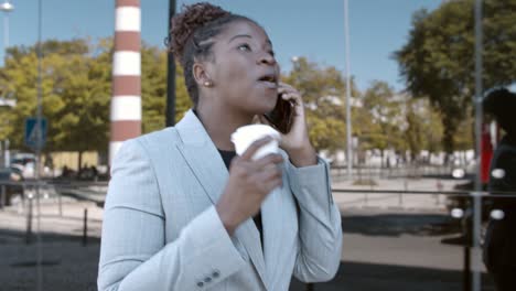 dolly shot of a smiling african-american businesswoman walking outside, holding coffee and talking on mobile phone