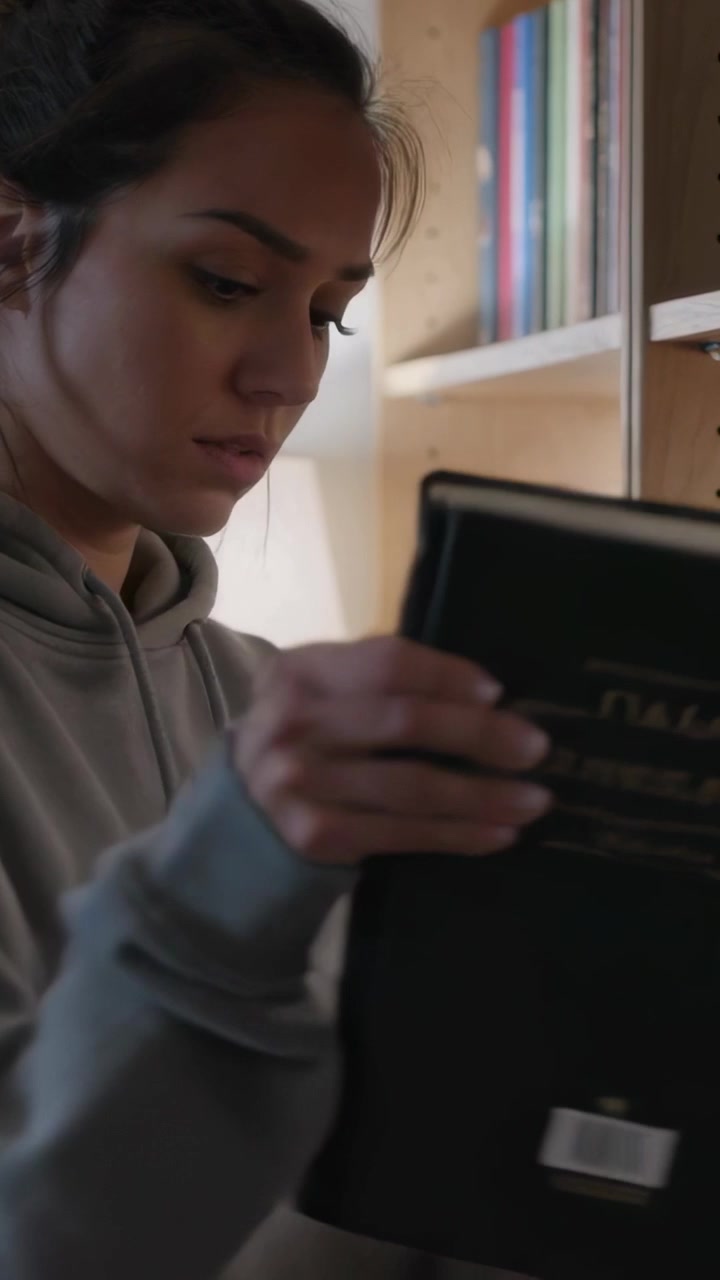 Vertical video: Scanning bookshelf Asian woman in gray hoodie pulling book at study to scan barcode