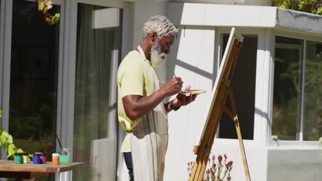 senior african american man painting picture on a canvas in sunny garden