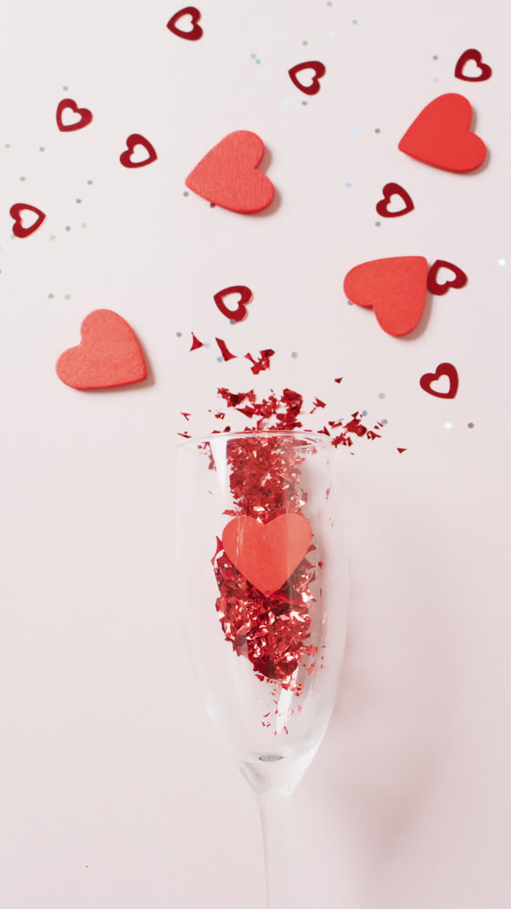 video verticale di bicchiere di champagne con cuori rossi e confetti, su sfondo bianco con spazio di copia