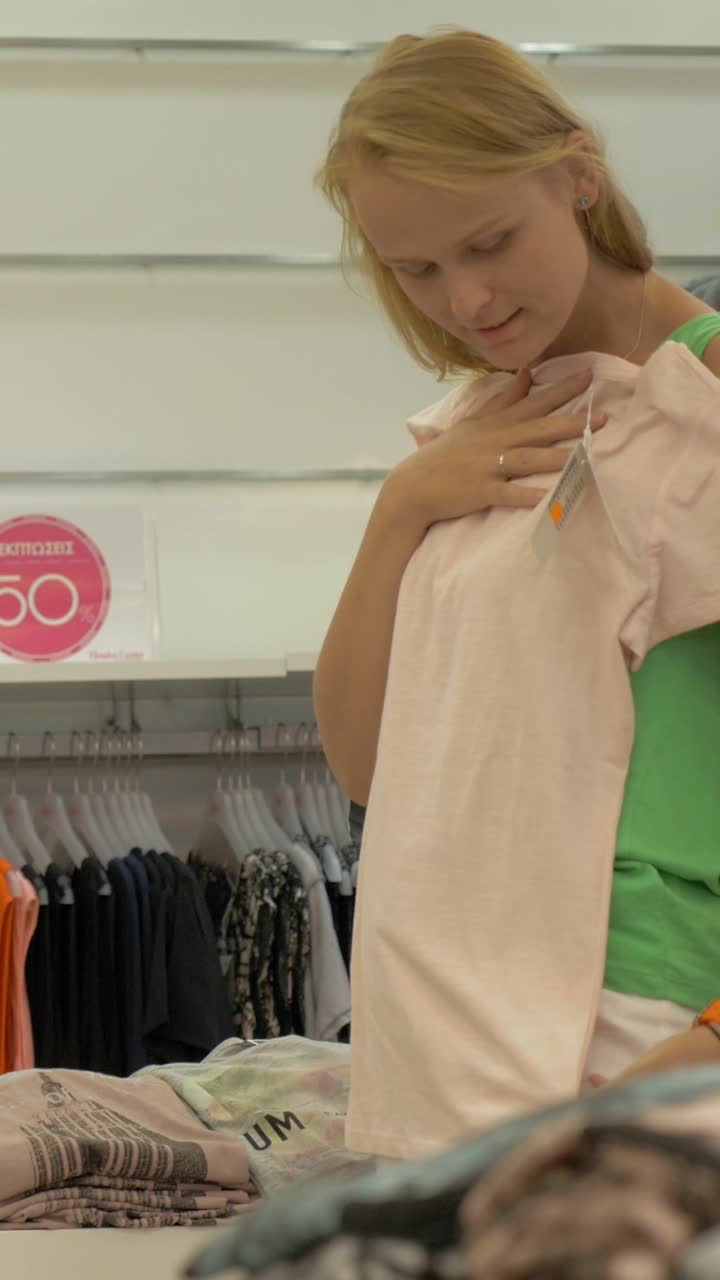 Giovane donna che guarda ed esamina vestiti in un negozio di abbigliamento.