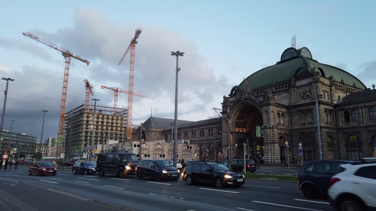 Outside view camera pan of Nuremberg station (old historic building) and a big construction site nearby. Many yellow cranes and cars.