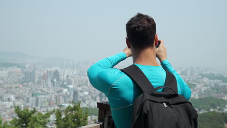 男のハイカーは ⁇ 霧の日にグワンカン山の頂上に立ってスマホを使ってソウルスカイラインの写真を撮っています ⁇