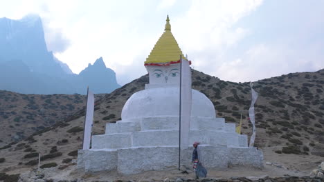 drone view of a sherpa woman performing religious ritual around a buddhist stupa at dingboche, everest trek. himalayas and peaks in the backdrop, gentle wind adds to the scene nepal tourism