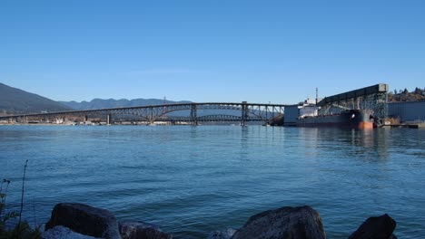 calm waters with a view of vancouver's industrial harbor and bridge against a mountain backdrop, clear day