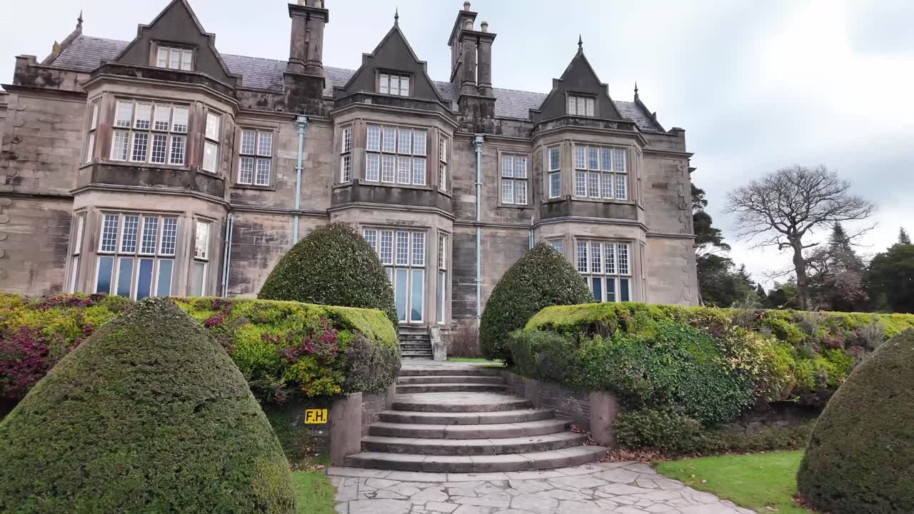 Trimmed shrubs, staircase and grandiose facade of Muckross house, national park Killarney, Ireland. Tudor style architecture
