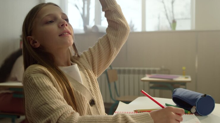 Cheerful girl studying in classroom. Cute schoolgirl writing in notebook