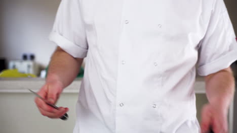 professional male chef sharpening a knife with a steel in his chef whites ready to cook a gourmet meal, then checks with his thumb to make sure it's sharp