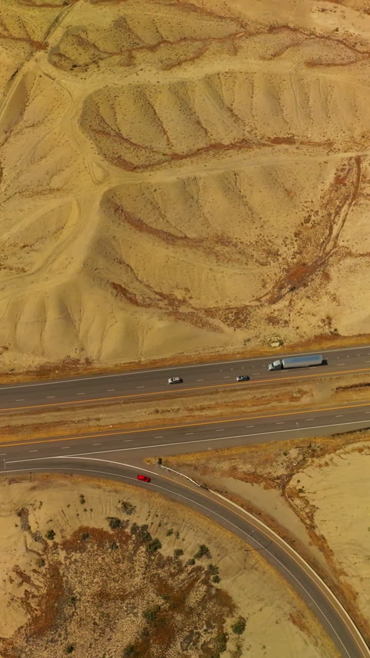 Sandy dunes crossed by the quick highways. Cars going fast by the roads of Colorado, USA. Aerial view. Vertical video