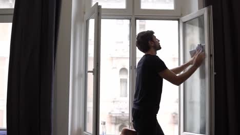 houseman is cleaning window, cleans surface, uses a rag, standing in modern apartment