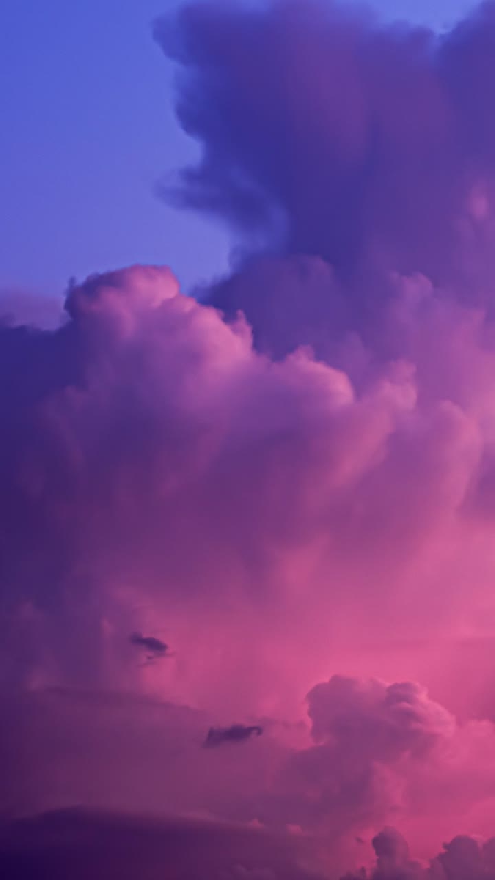 Colorful storm clouds in vivid pink and purple hues drift and swirl in a vertical timelapse shot