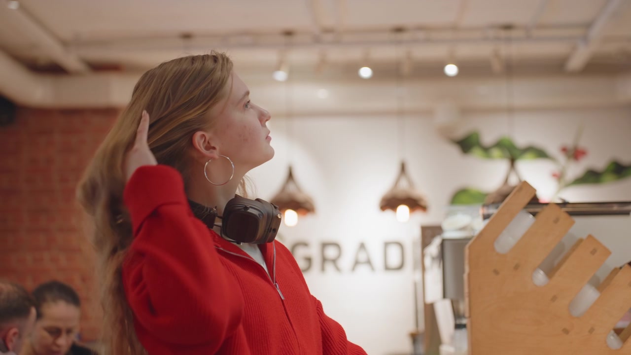 Tankefuld ung kvinde med hovedtelefoner på en moderne café