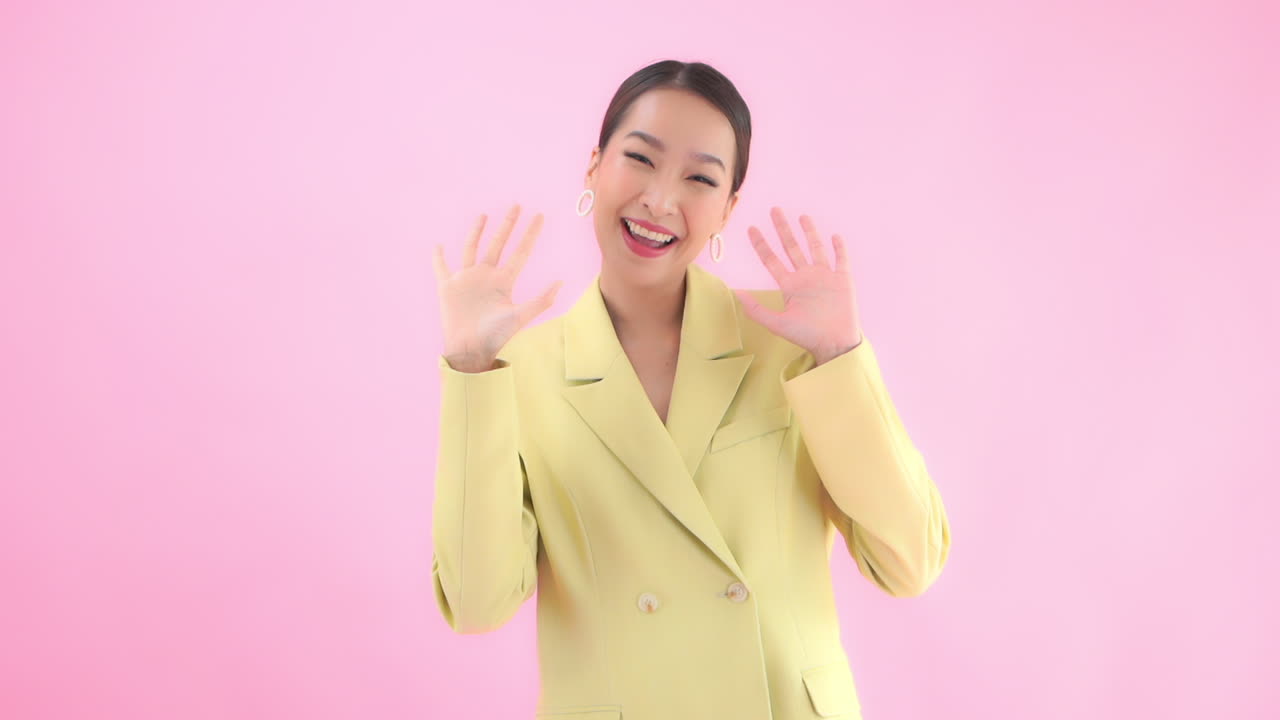 Smiling girl portrait in the Studio in a yellow business suit waving goodbye. Isolated on pink