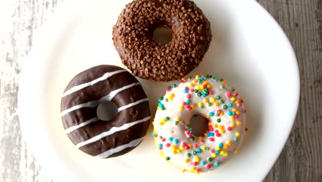 tres deliciosas rosquillas dulces girando en un plato. mesa de madera rústica. en bucle