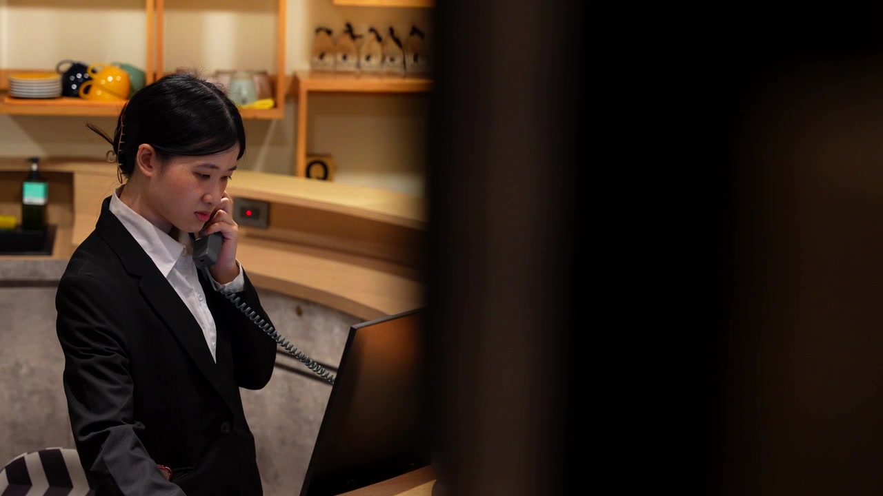 Concierge professionista donna alla reception dell'hotel che risponde a una telefonata e controlla un computer.