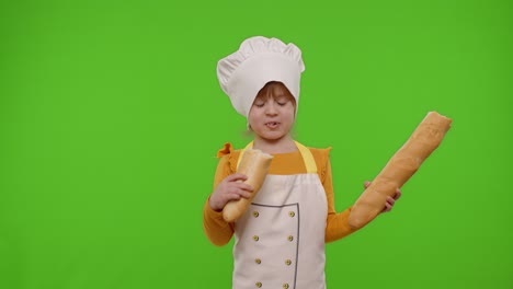 niña niña vestida con delantal y sombrero como chef cocinero comiendo baguette fresca y sabrosa, haciendo tonterías