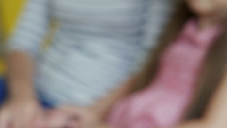 Blurred-Portrait-Of-Cute-Girl-Sitting-With-Her-Mother-On-The-Couch-And-Then-Smiling-To-The-Camera