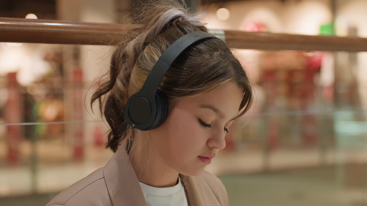 쇼핑몰에서 멜로디를 즐기는 젊은이, 쇼핑몰 주변을 둘러보면서 음악에 몰두하는 젊은이, 쇼핑센터 분위기 속에서 귀를 덮는 헤드폰으로 음악 경험을 즐기는 청소년