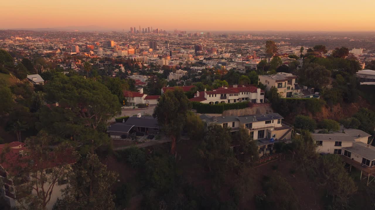 Riprese da drone sopra le case di Hollywood Hills con lo skyline di Los Angeles sullo sfondo al tramonto.