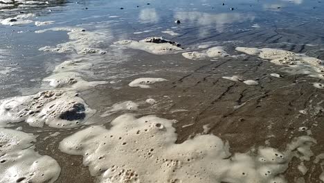 Espuma-De-Mar-Sucia-Moviéndose-Lentamente-A-Través-De-La-Playa-De-Arena-Galesa-Con-Olas-De-Marea