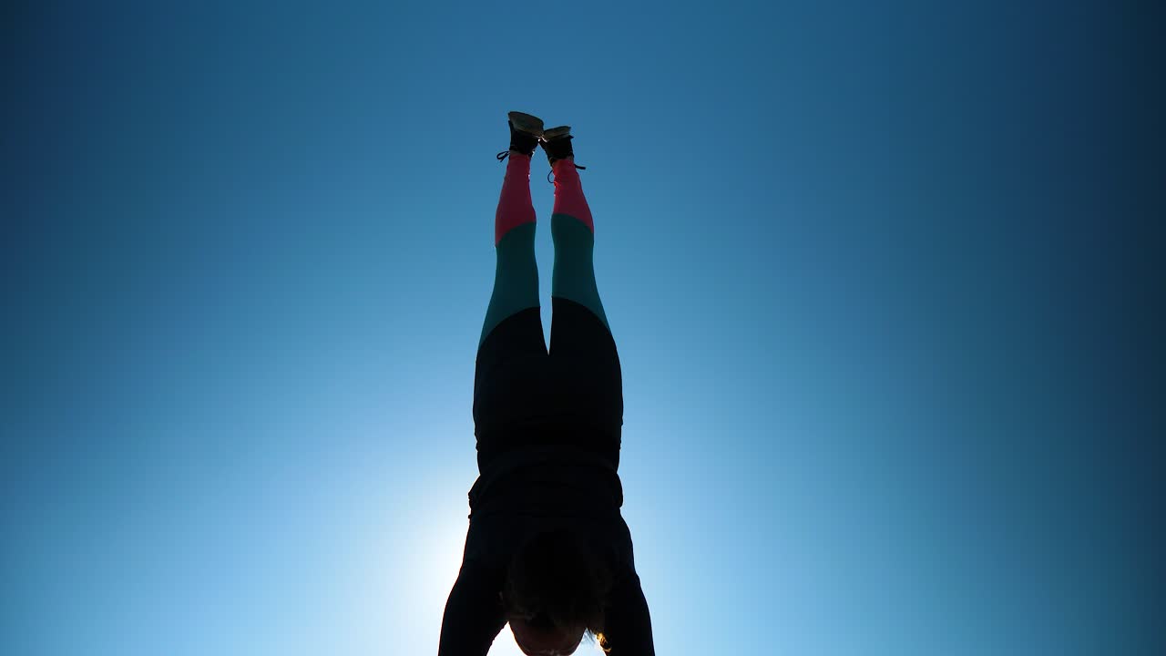 Young athletic girl does handstand and split in front of camera and sun