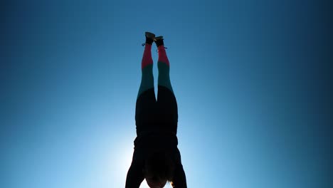young athletic girl does handstand and split in front of camera and sun