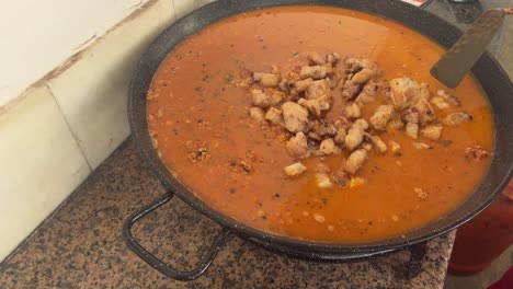 person is cooking food in big metal pan, using steel cooking spatula