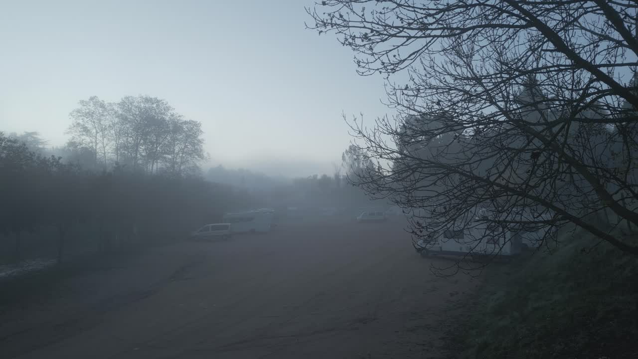 Morning fog gradually envelops a camper van parking area in catalonia, spain, creating a serene and slightly mysterious atmosphere as the landscape slowly disappears into the mist