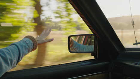 woman holding hand out car window feeling wind blowing through fingers driving in countryside travelling on summer vacation road trip enjoying freedom on the road