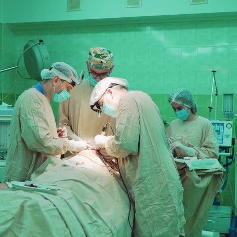 teamwork of professional surgeons in the operating room. doctors in special uniform work with medical equipment during the operation on a patient on the green background in clinic.