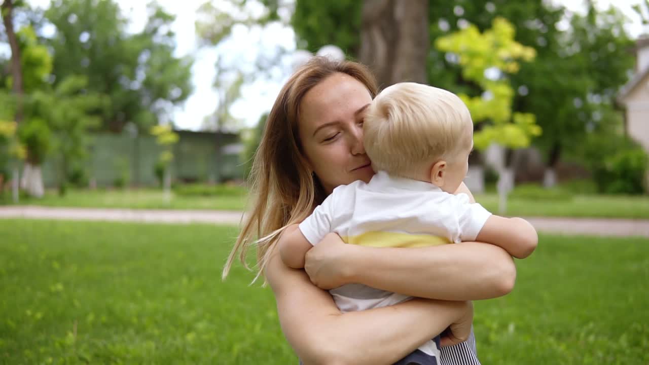 pequeño niño rubio corriendo hacia su madre. mamá abrió las manos y sonriendo atrapa al bebé. madre feliz, hijo amoroso. picnic al aire libre. parque verde. cámara lenta