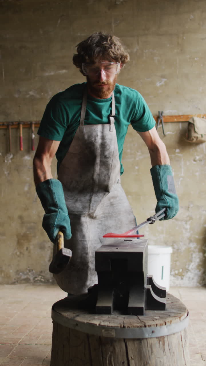 video vertical de un herrero caucásico forjando metal caliente con un martillo en el yunque en el taller