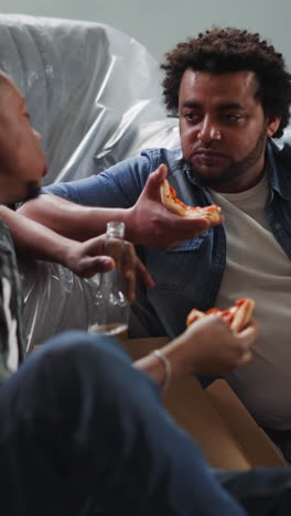 african-american guys eat talk and relax sitting on floor in renovated room. young black men celebrate repairing finish in new house. domestic party