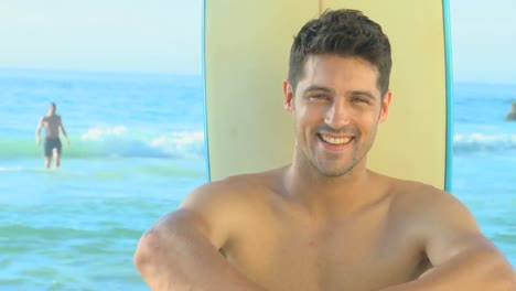 Handsome-man-posing-in-front-of-a-surf-board