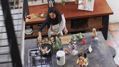 mujer biracial preparando comida usando una tableta en la cocina, cámara lenta