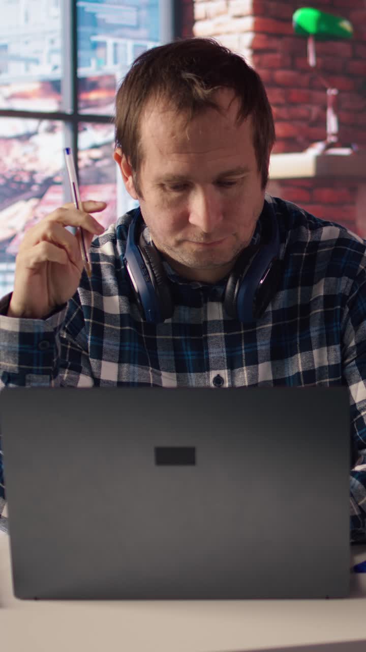 Vertical video Stressed man in home office scratching head with pen, feeling overworked