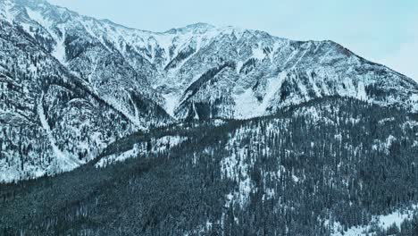 aerial wide approach to winter landscape with snow covered mountain ridges and evergreen forests, isolated wilderness