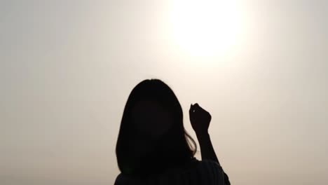 Silhouette-Eines-Asiatischen-Mädchens,-Das-Ihre-Hand-In-Richtung-Sonne-Hebt,-Ihre-Faust-Ballt-Und-Ihre-Hand-Nach-Unten-Legt