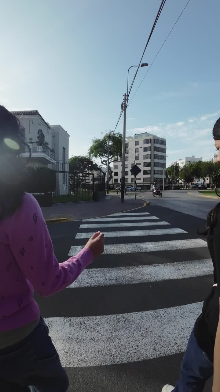 Due persone che attraversano un passaggio pedonale in una strada urbana soleggiata